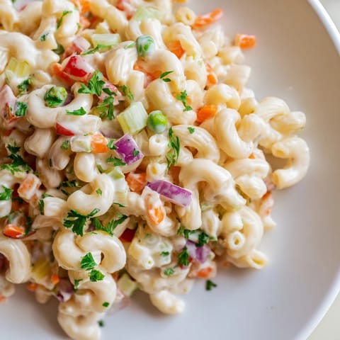 A picnic-perfect bowl of macaroni salad, featuring vibrant red peppers and a tangy dressing.