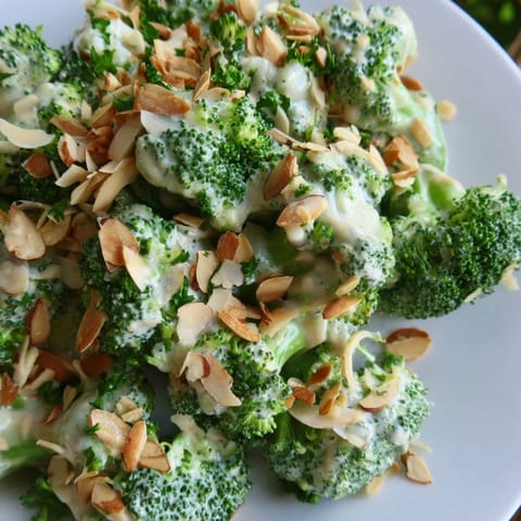 A close-up of vibrant green Garlic Parmesan Broccoli Salad in a white bowl, featuring crisp blanched florets tossed in creamy dressing and topped with toasted slivered almonds.