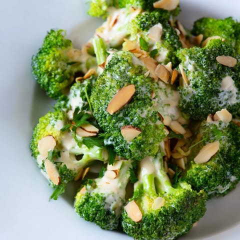 Freshly prepared Garlic Parmesan Broccoli Salad shows bright green florets mixed with red onion and optional cherry tomatoes, garnished with parsley and extra grated Parmesan.