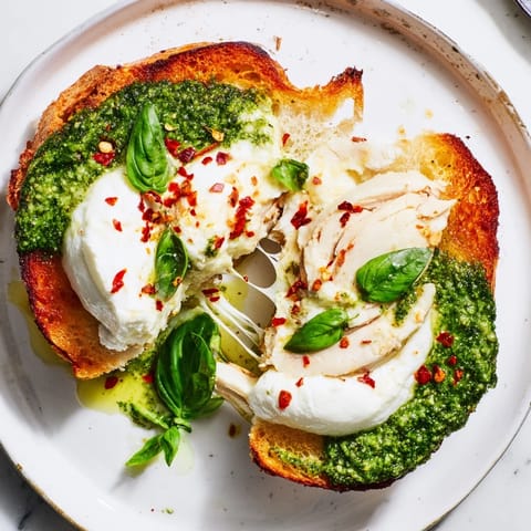 Golden toasted sourdough topped with creamy burrata and pesto chicken slices, garnished with fresh basil.  