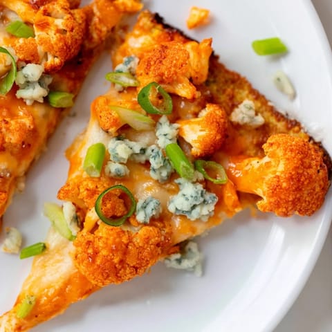 Golden Buffalo Cauliflower Pizza slices topped with blue cheese crumbles and parsley, ready to serve for a spicy vegetarian dinner.