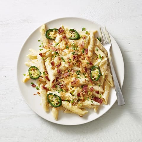 A close-up of cheesy Jalapeño Popper Pasta, garnished with toasted panko breadcrumbs and fresh chopped chives.