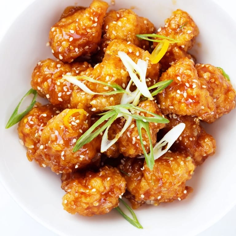 This homemade Orange Chicken features tender chicken enveloped in a flavorful, glossy orange sauce with visible garnishes.