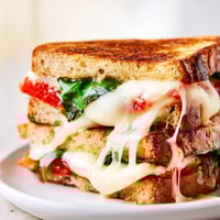 Two slices of tomato basil grilled cheese rest on a cutting board, showcasing melted mozzarella and fresh basil between golden sourdough bread.  