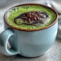 A warm, creamy black sesame matcha latte with frothy milk and a marbled swirl of nutty black sesame paste.  