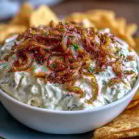Creamy caramelized onion dip with Greek yogurt base, garnished with fresh chives, served with crispy potato chips.  