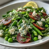 Bright lemon vinaigrette spring salad with radishes and peas in a white bowl, garnished with chives and feta, perfect for a light lunch.