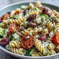 A colorful bowl of summer pasta salad with olives, feta, and fresh vegetables in a light Mediterranean dressing.